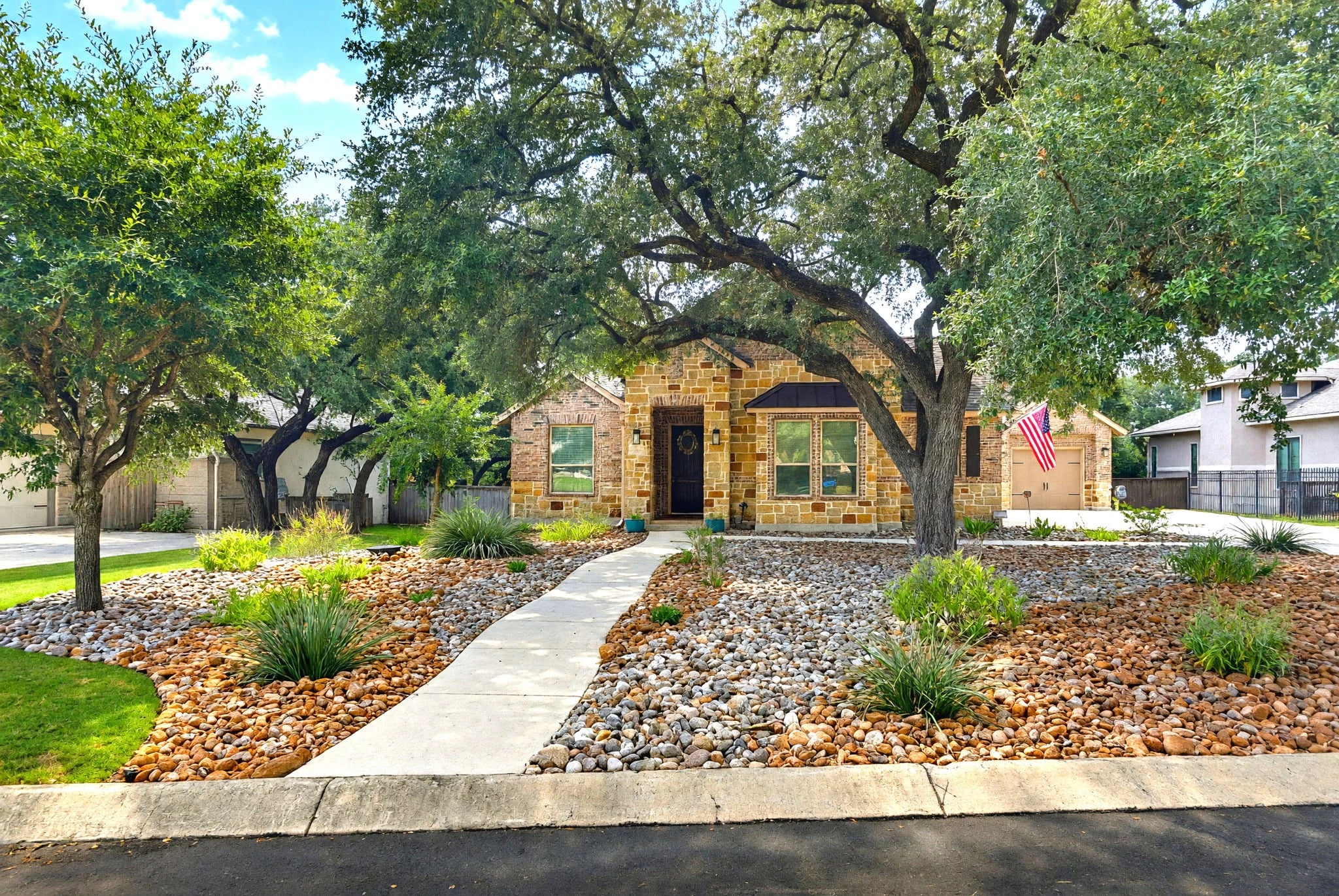 A stone Texas Hill Country home behind a live oak, with a walkway to the front door